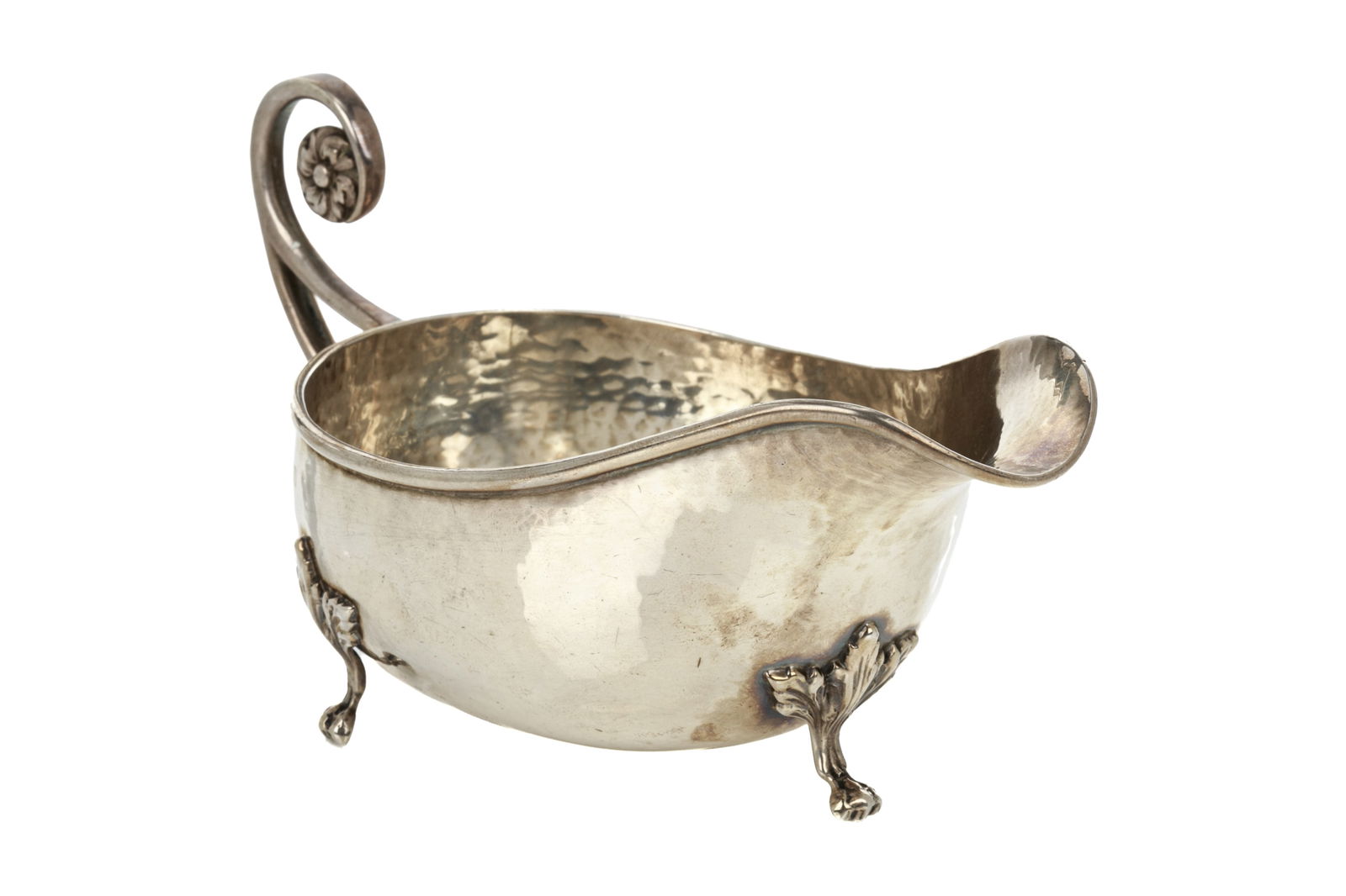 ARTS AND CRAFTS SILVER SAUCE BOAT, 153g: An early 20th century sterling silver sauce boat in the Arts and Crafts style by AE Jones, Birmingham 1920. The hammered body has applied feet with a leafmotif and the handle has a cast flower as a fi