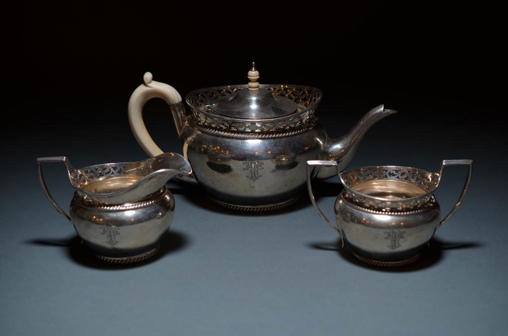 ENGLISH SILVER THREE PIECE TEA SET: An English sterling three piece tea set. Maker Charles Stuart Harris London 1921. Each piece in low round form surmounted with a pierced gallery. The tea pot fitted with an ivory finial and handle. 10