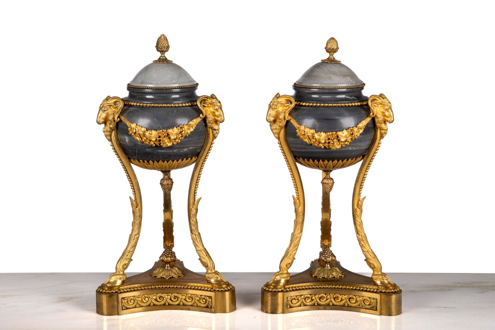 PAIR OF FRENCH GREY MARBLE AND BRONZE URNS: Pair of dark slate-coloured marble urns with bulbous bodies raised on three ormolu hoofed-feet capped with ram's heads and swag details across the body. French, 19th C. H.: 46 cm (18 in.)
