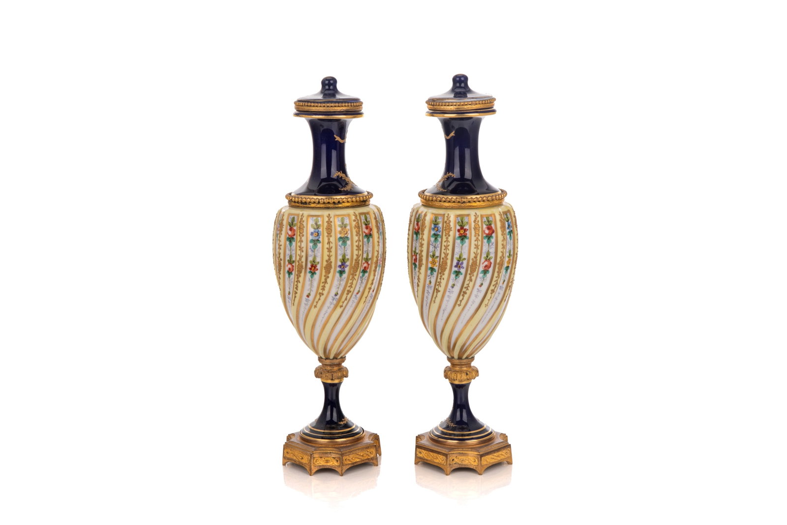 PAIR OF FRENCH PORCELAIN GARNITURES: Two Sèvres-style porcelain garnitures with rich cobalt ground, twisting fluted bodies, hand-painted gilding and foliate designs throughout, and set on bronze mounts. Mark in blue to base shows the in