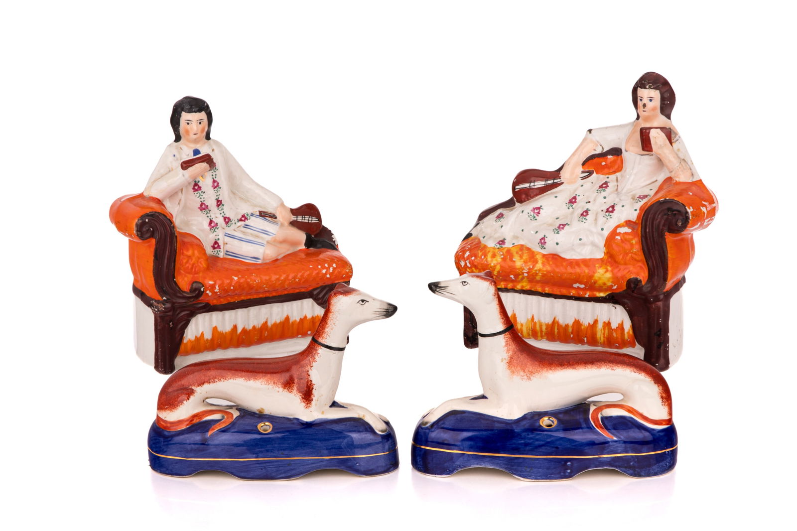 TWO PAIRS OF STAFFORDSHIRE POTTERY FIGURES: Four English Staffordshire pottery figures hand-painted in brightly-coloured polychrome. Including one pair of figures reclining on a chaise with a book and one pair of quill holders in the shape of h