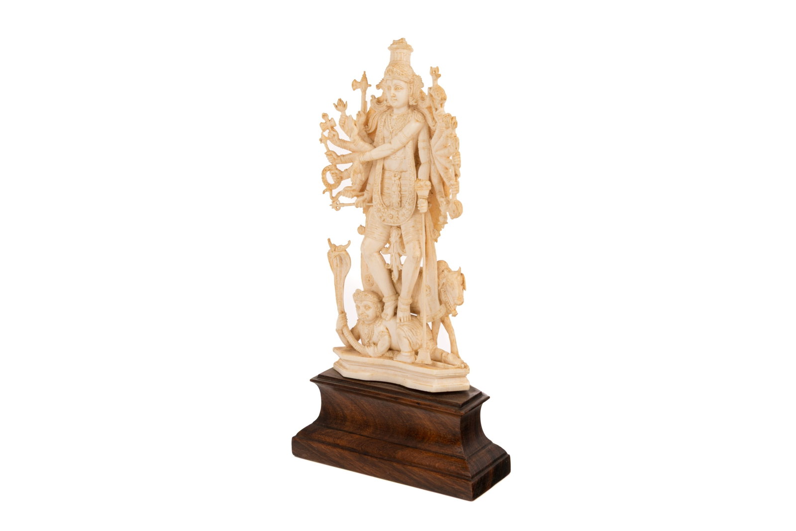 INDIAN STANDING CARVED VISHNU DEITY: Carved long haired Vishnu with sixteen arms and each holding a different object, stepping on King Bali who is holding a serpent, and in front of a ram. On hardwood stand. H. with stand: 26 cm (10.25 i