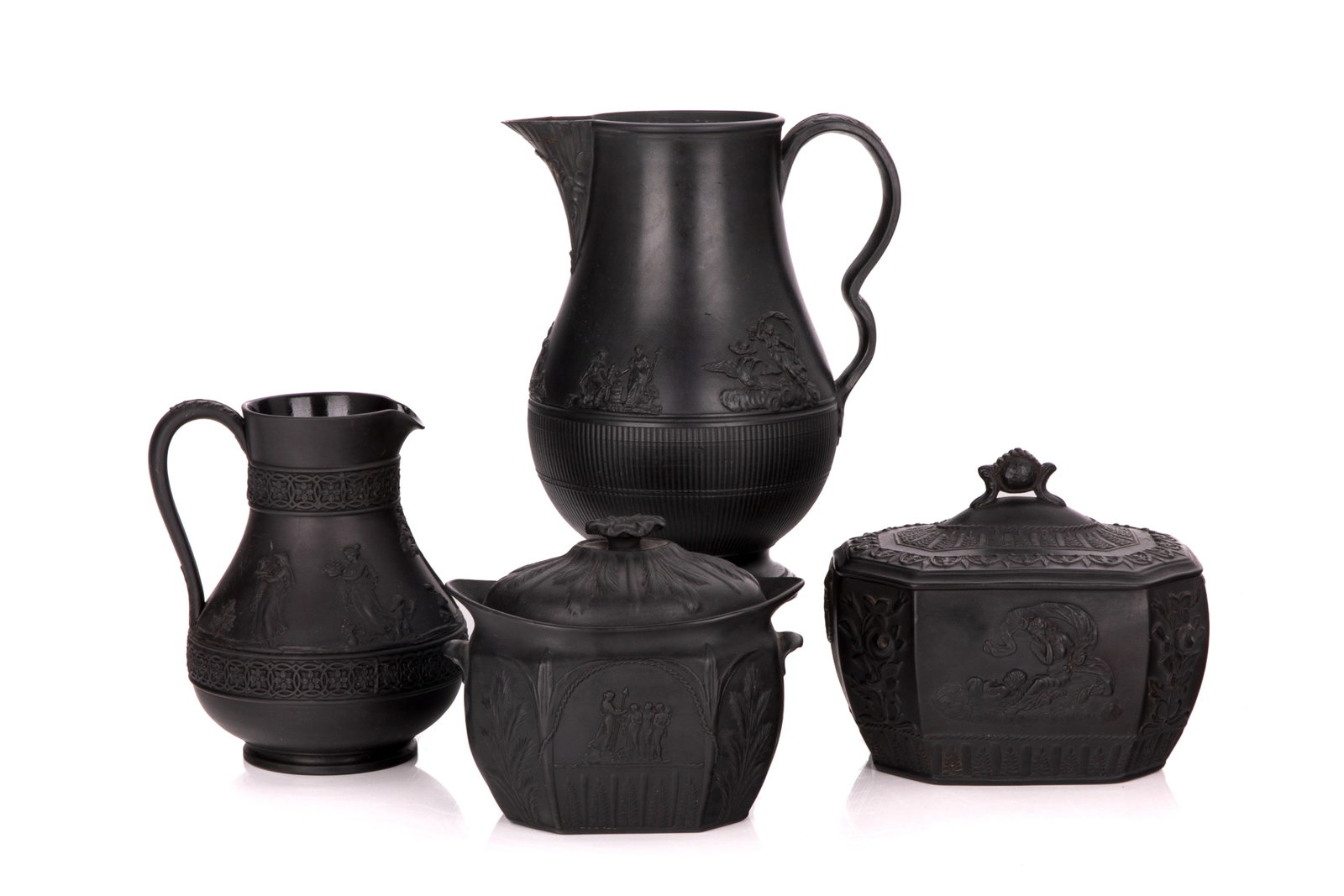 FOUR PIECES OF 19th C BLACK BASALT: Two black basalt covered sugar bowls in the Wedgwood style with Neo-Classical figures and motifs in relief and two jugs (repair to one spout). English, 19th C. L. of larger: 15.5 cm (6 in.)