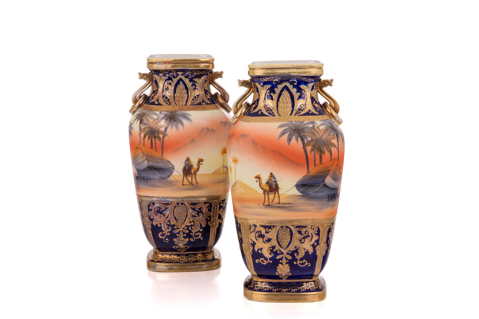PAIR OF NIPPON PORCELAIN EGYPTIAN MOTIF VASES: Two handled vases with dessert scene with camel and palm trees, cobalt border. Height 12.25 in 31 cm