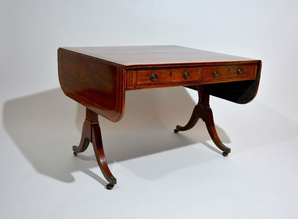 REGENCY ROSEWOOD SOFA TABLE: Rounded rectangular drop leaf top with mahogany and fruitwood banding and ebony stringing, original circular escutcheons and hardware, English, circa 1810. 62 x 34 x 28 in.
