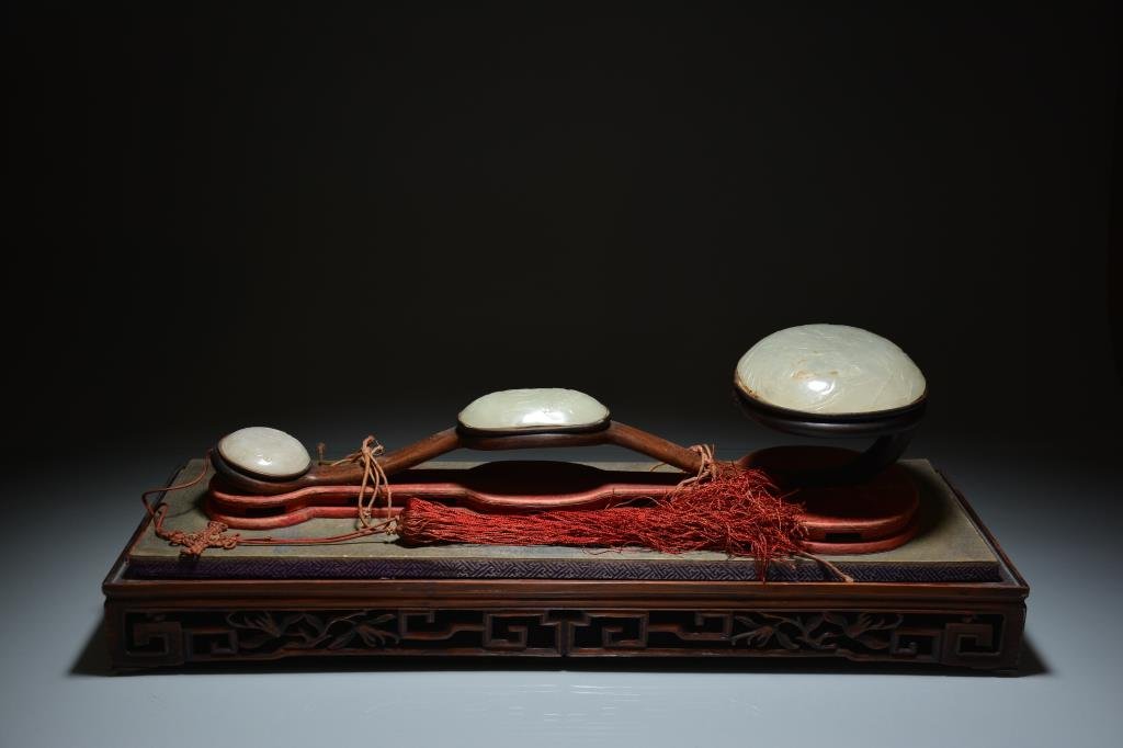 FINE HARDWOOD & JADE RUYI SCEPTER: Huanghuali wood scepter with three finely carved light celadon jade plaques of immortals amongst trees and mountains. Original silk stand with tassels and original carved wood case. L of scepter 56 cm