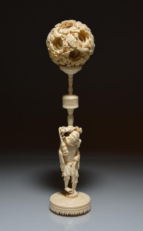 CHINESE LARGE CARVED IVORY PUZZLE BALL: The stand is carved in the form of Daoist immortal Li Tieguai holding a double-gourd vase from which a stream of clouds emerge to support the dragons-decorated puzzle ball, base is carved with dragons