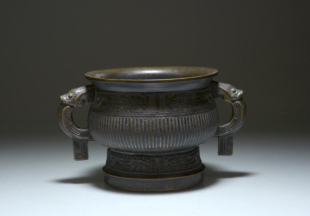 CHINESE ARCHAISTIC BRONZE VESSEL, GUI: Of western Zhou ritual food vessel shape; neck and pedestal foot have bands of stylized qilins against scrolling clouds, with ribbed body and bovine-mask loop handles, centre has archaistic writings.1