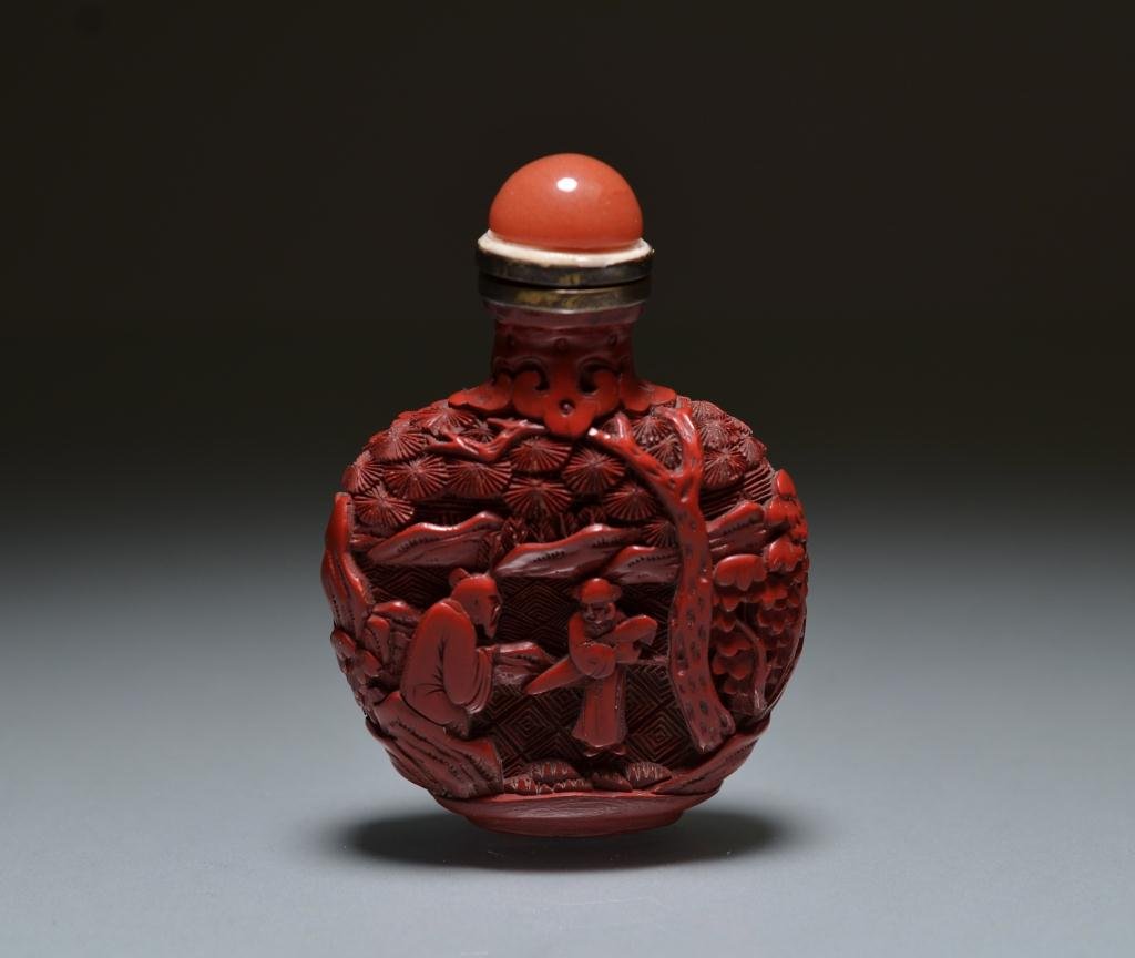 CHINESE CINNABAR LACQUER SNUFF BOTTLE: Oval form, decorated with elders and attendant in landscape; carnelian stopper. 19th century or earlier. H. 8.2cm (3 1/4 in.)