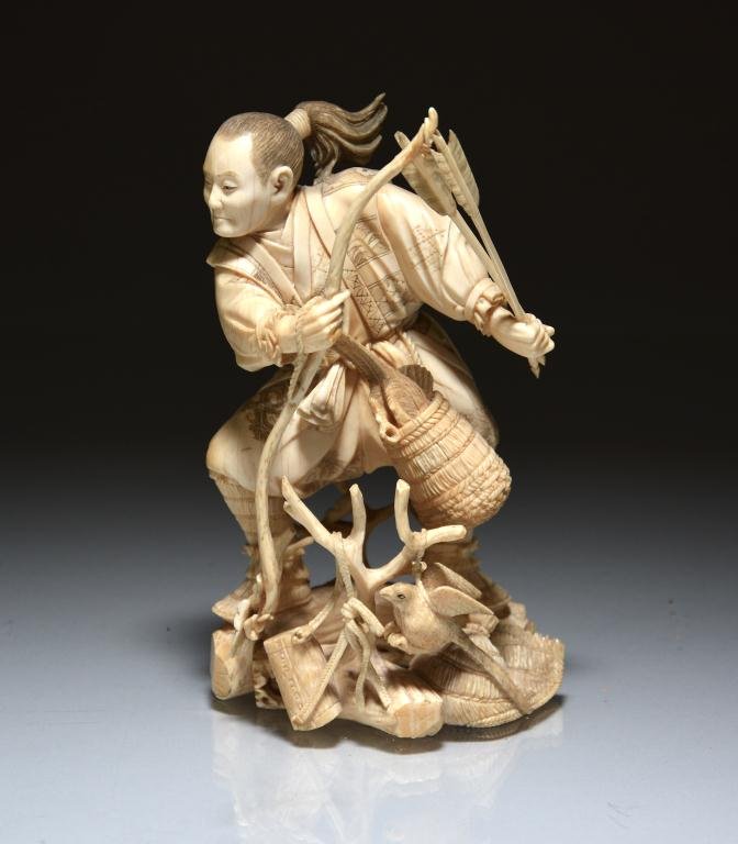 JAPANESE IVORY OKIMONO OF A HUNTER: Finely carved as a hunter man grabbing a bow and arrow, his quarries are tight to a tree trunk and in a woven basket tight to his belt; signed "Gyoku," Japanese, Meiji. H. 15.5cm (6 1/7 in.) DISCLAIME