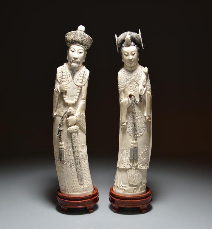 CHINESE CARVED IVORY FIGURES OF EMPEROR & EMPRESS: The emperor wears a court necklace and carries a sword, the empress holds a scepter. Qianlong mark to base. On carved fitted wood stands. H. 37cm (14.5 in.) DISCLAIMER: This item is restricted from ex