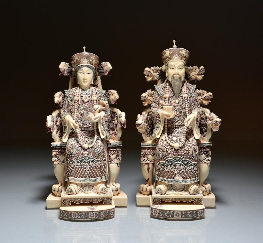 CHINESE CARVED IVORY FIGURES OF EMPEROR & EMPRESS: Both dressed in imperial robes and sitting on dragon thrones, the emperor holds a packet and the empress with a scepter. On fitted carved wood stands. H. 24.5cm (9 3/4 in.) DISCLAIMER: This item is re