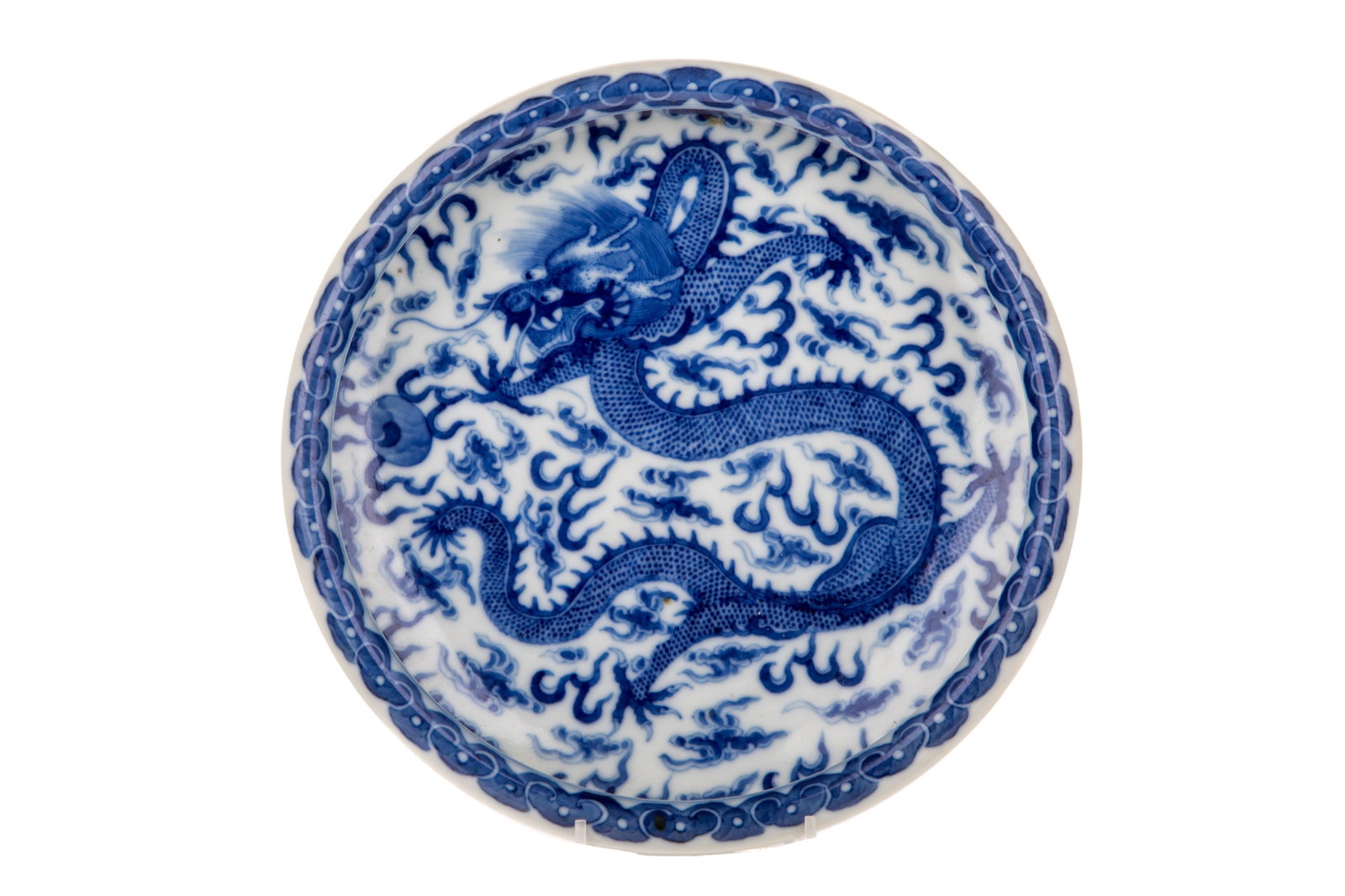 CHINESE BLUE& WHITE DRAGON LOW BOWL: The cavetto decorated with a five-clawed dragon chasing a flaming pearl, the rim with a ruyi band. The reverse with waves surrounding the foot ring, with a six-character Kangxi mark. Diam. 23 cm