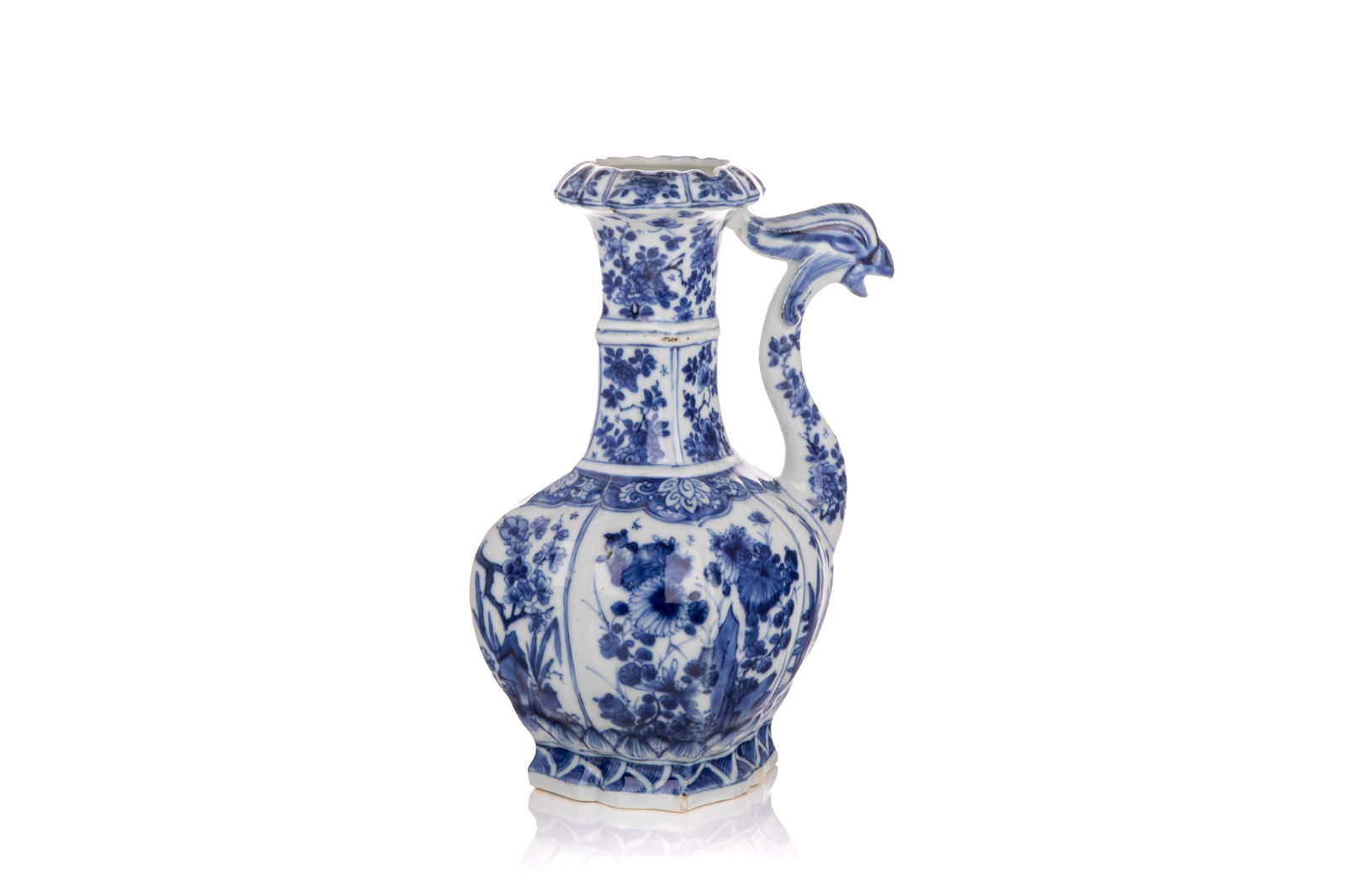 KANGXI BLUE AND WHITE PHOENIX HEAD EWER: A foliate diamond section, with a high banded neck and phoenix head spout. Floral panels throughout, and molded lotus lappets at the base. Qing dynasty, Kangxi (1662-1722). Compare similar ewer with o