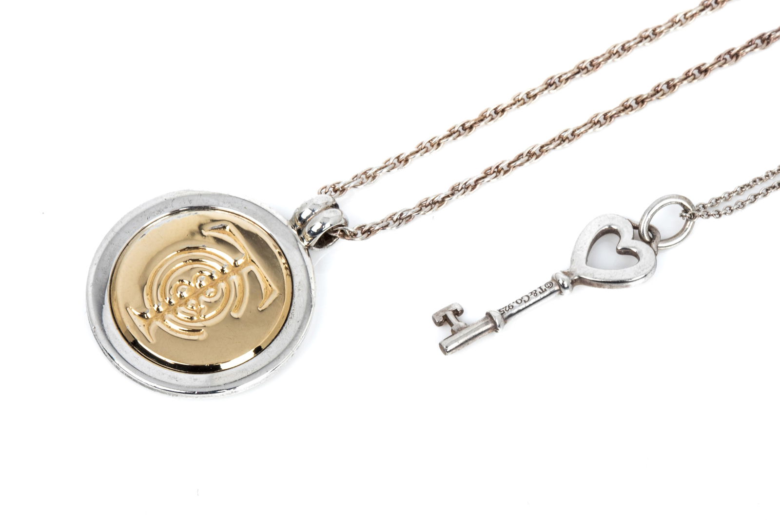 STERLING SILVER TIFFANY & CO. NECKLACES 17.1g: Sterling silver and 18K yellow gold T&C coin medallion pendant measuring 30.0mm long by 24.5mm wide, stamped TIFFANY & CO. 925/750. Accompanied by 18 inch long 1.9mm wide sterling silver