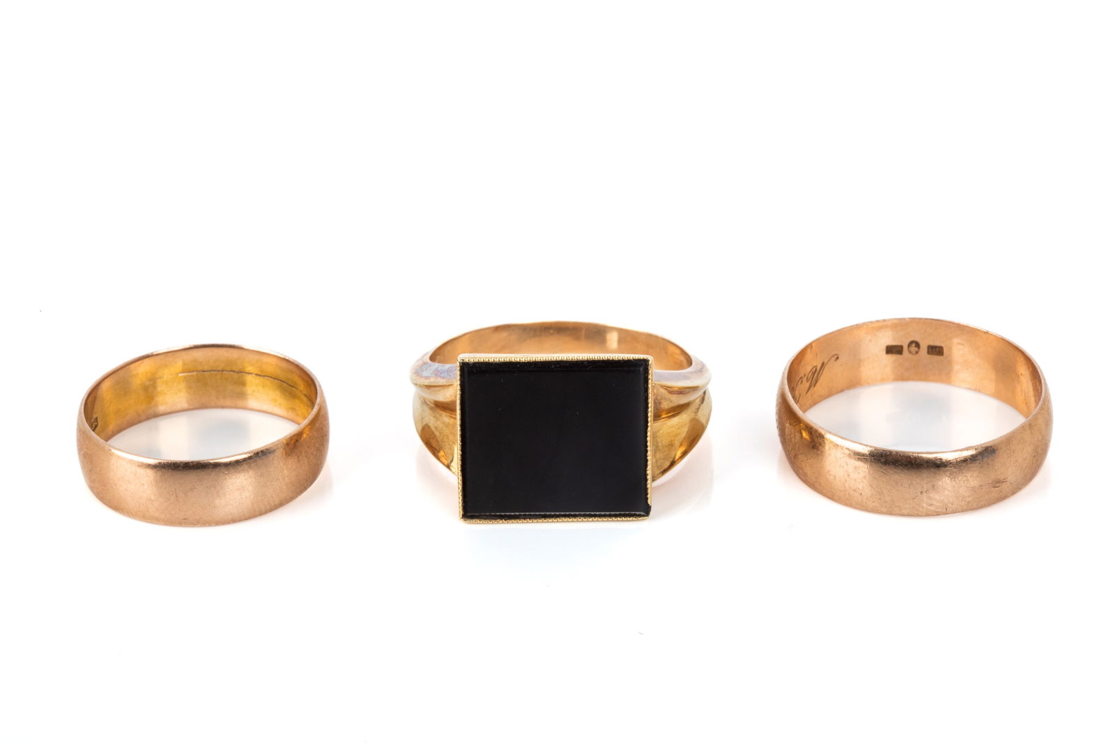 TRIO OF 14K GOLD RINGS 12.7g: 14K yellow gold signet style ring measuring 13mm wide by 4.8mm tall, featuring a bezel set rectangular onyx. Size 10.56 grams 2 14K rose gold plain bands measuring 5.7mm wide. Sizes 7.25 and 9.75 Both
