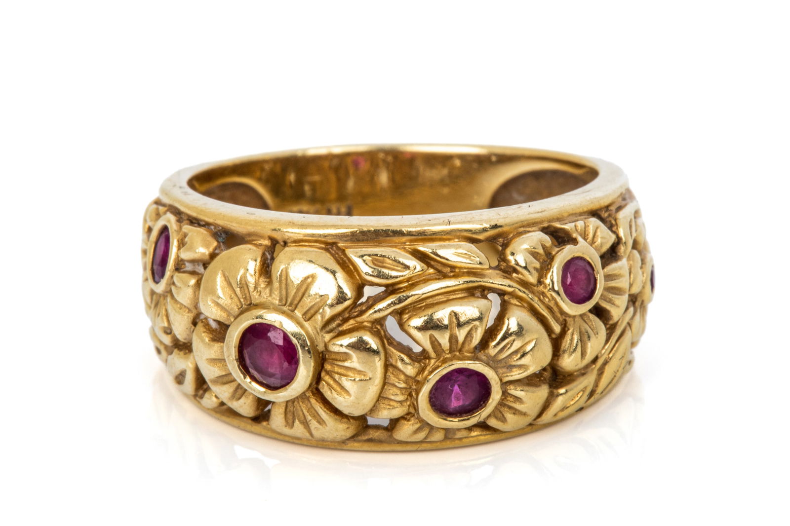 18K RUBY FLORAL BAND 10g: 18K yellow gold floral band measuring 11.2mm wide Featuring 5 round faceted strongly purplish red rubies of varying sizes Size 9