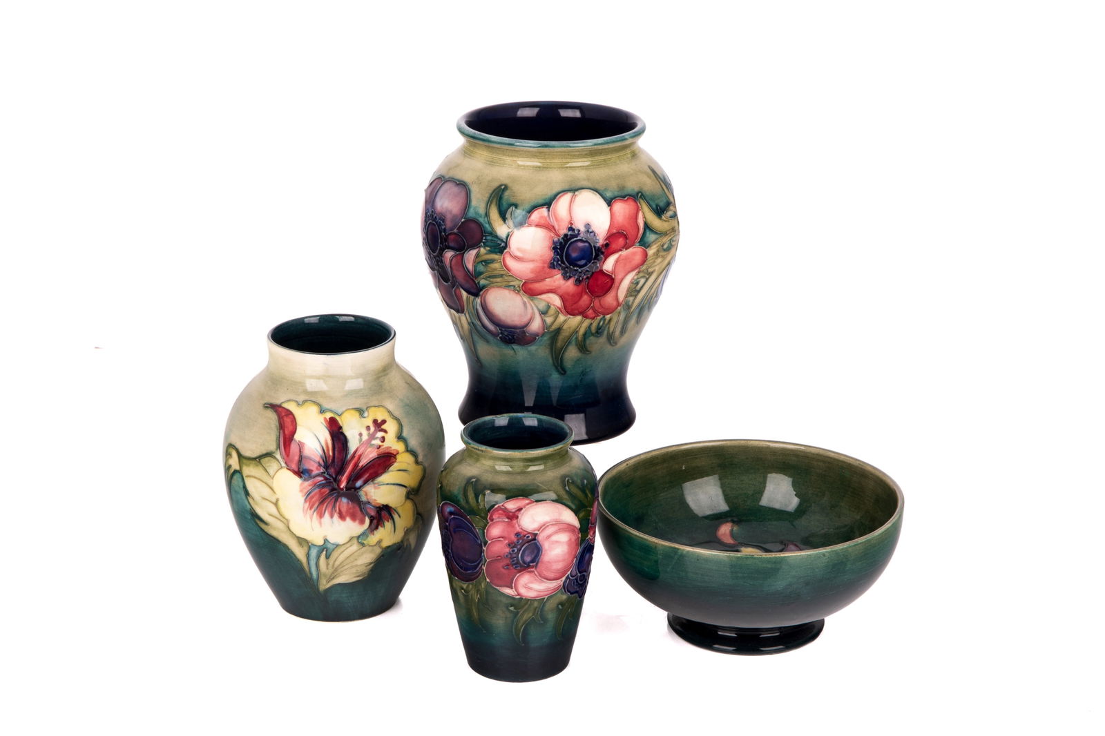 FOUR PCS OF MOORCROFT POTTERY: Each designed with a pale green to dark teal ombre and painted with varying flowers of magenta, red, and violet. Includes three vases and one footed bowl. Hibiscus and Anemone patterns. Tallest