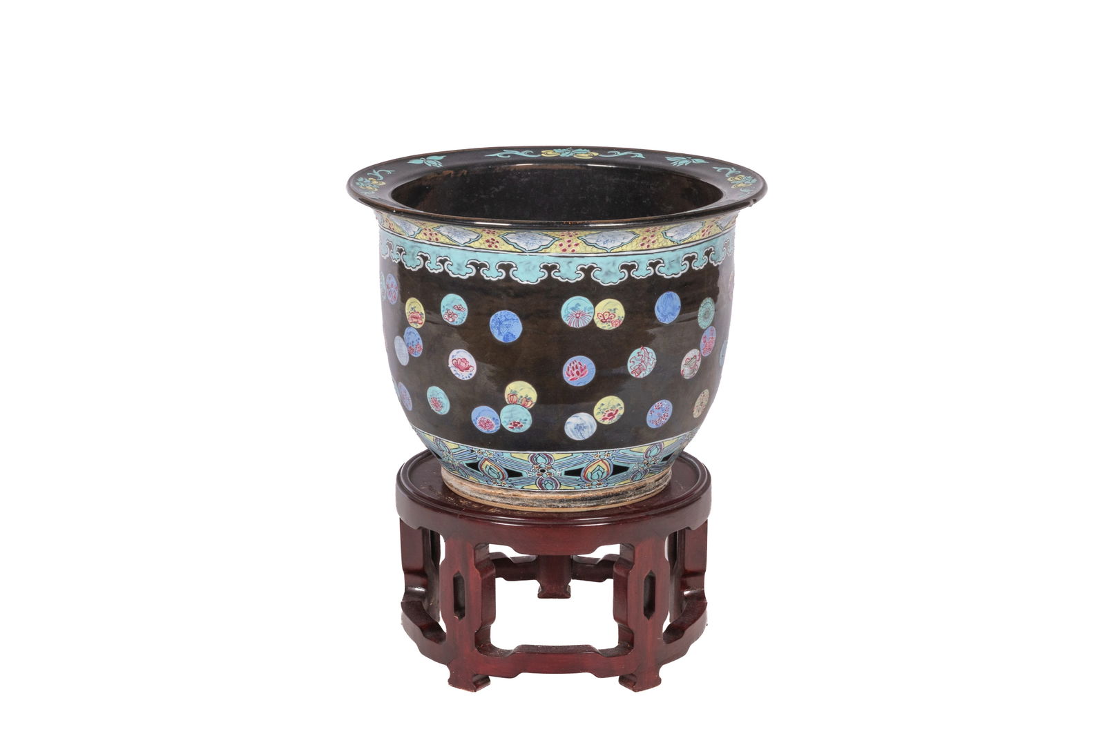 FAMILLE NOIRE ROULE DECORATED JARDINIERE AND STAND: The body decorated with ornate medallions on a black ground. On carved wood stand. Xuantong to Tongzhi period, late 19th century. Diam. 40.5 cm; H. (without stand) 30 cm, (with stand) 48.5 cm