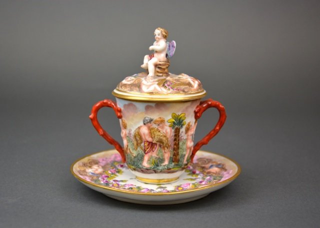 Capodimonte porcelain covered cup & saucer: - chocolate cup with putti motif and red handles *condition to finial, late 19th/early 20th cen.