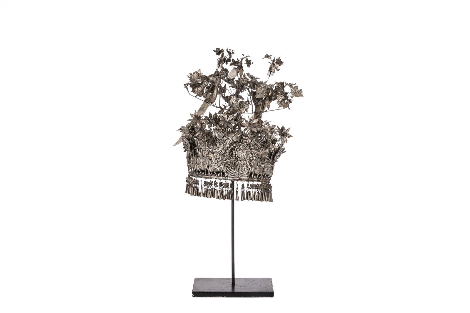 CHINESE MIAO SILVER HEADDRESS: Decorated with peacocks amidst blossoming florals. The crown with a band of figures riding on horses with suspended charms. On metal stand. H. 38 cm