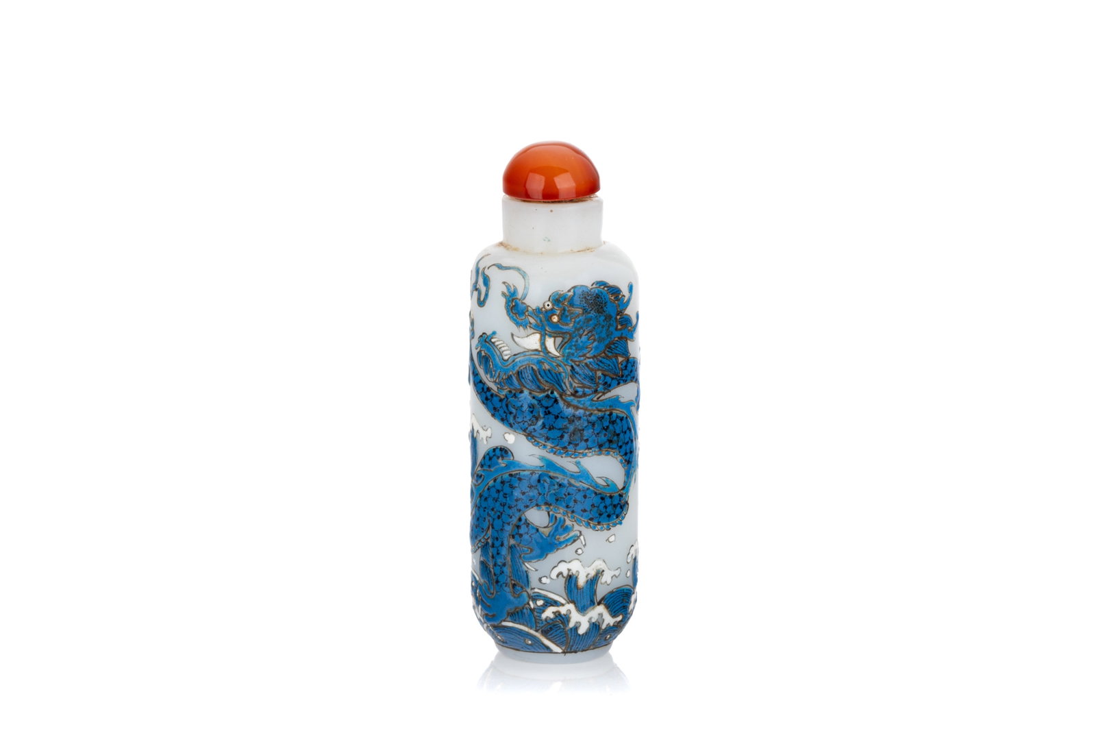 BLUE AND WHITE ENAMEL ON WHITE GLASS SNUFF BOTTLE: Of cylindrical form, the body painted with a five-claw dragon chasing a flaming pearl above crashing waves. Guyuexuan mark to the underside. Carnelian stopper. H. 8.5 cm