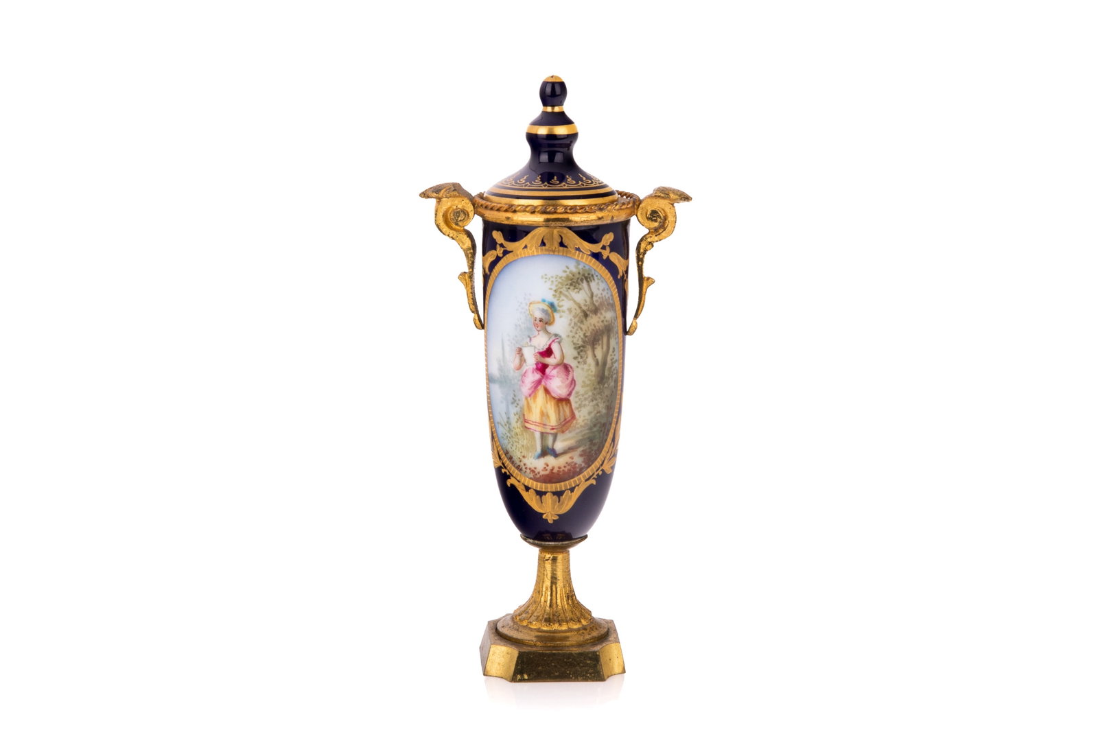 FRENCH SEVRES-STYLE MINIATURE URN: Slender cobalt blue body, an ornate removable lid with a golden finial, cast gilt bronze ormolu handles. Features a hand-painted motif of a classical pastoral romantic scene of a woman in traditional 