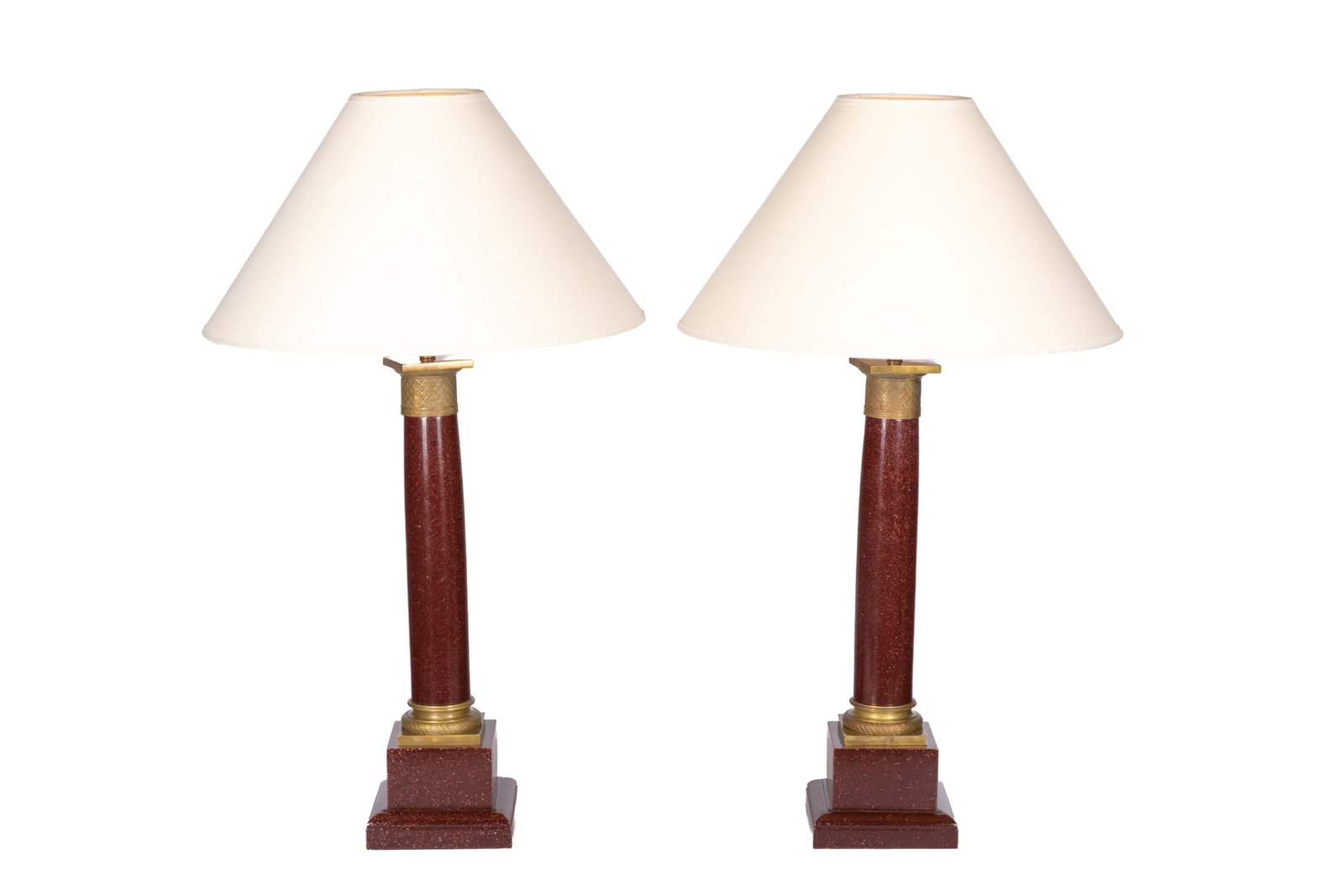 PAIR OF RED FAUX STONE TABLE LAMPS: A pair of Neoclassical style table lamps with an architectural column and a vibrant, mottled red shaft. The column is flanked at the neck by an embossed gilt-brass geometric band motif and rests upon 