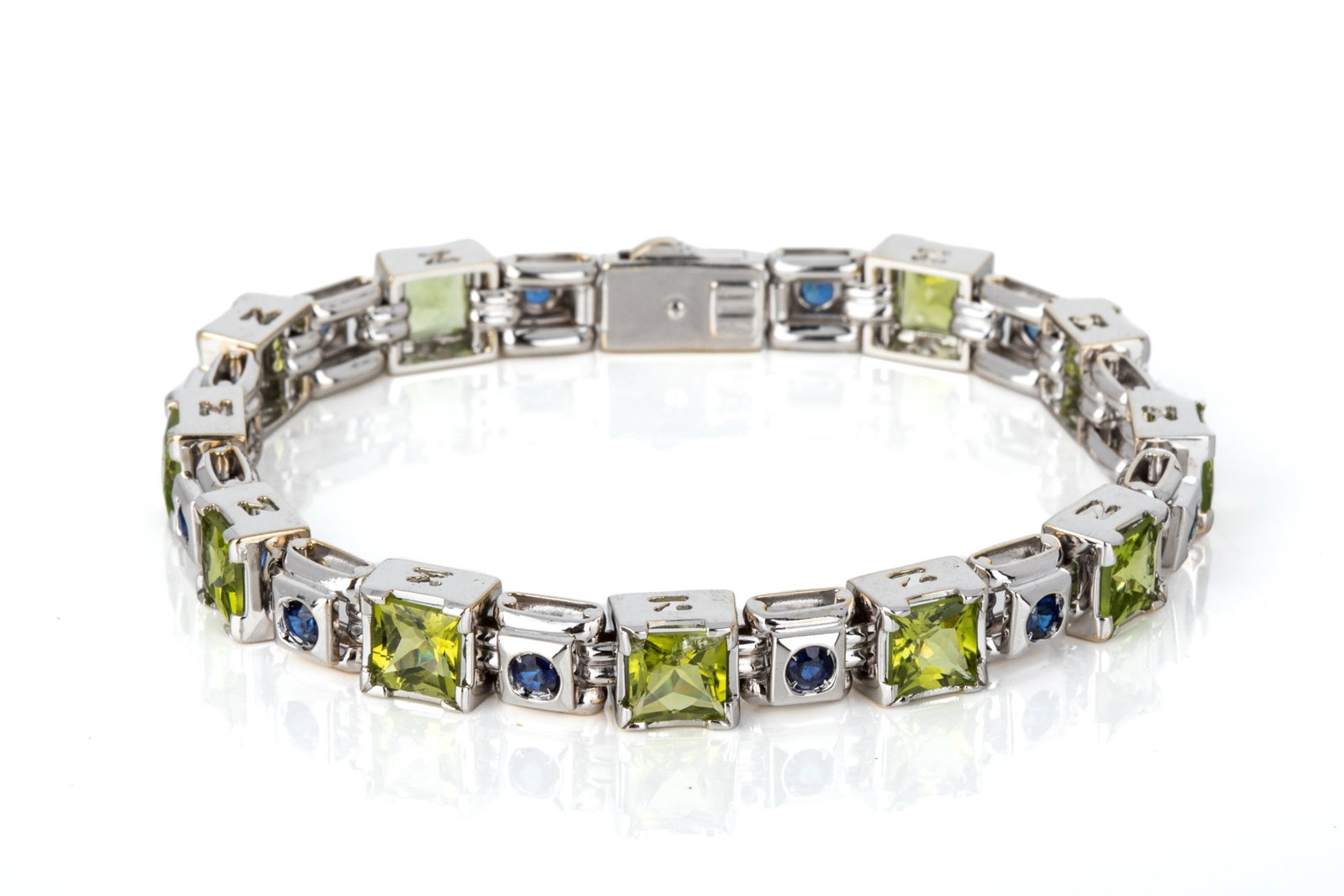18K ZANCAN ITALY PERIDOT & SAPPHIRE BRACELET 33.5g: 18K white gold bracelet by Zancan Gioielli, Vicenza, Italy. Measuring 7.75 inches long by 7.7mm wide by 5.5mm tall, equipped with heavy pull-trigger clasp. Featuring 11 square mixed cut peridot and 12