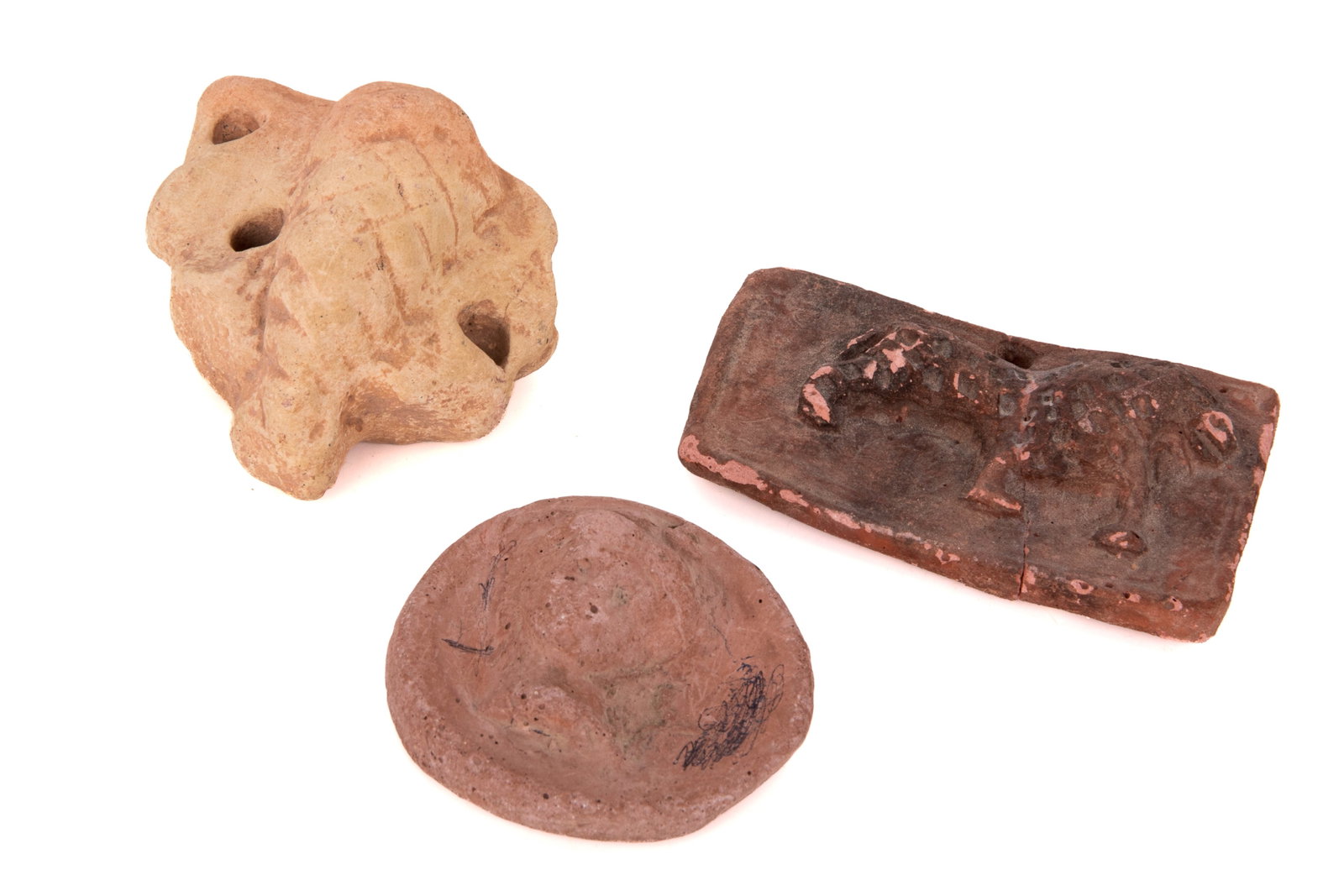 THREE ANCIENT TERRACOTTA ARTIFACTS: Including: -A rectangular mold-pressed plaque with an animal relief -A round stamped disc -A perforated ceramic fragment H 2 1/4in (6cm) x L 4in (10cm)