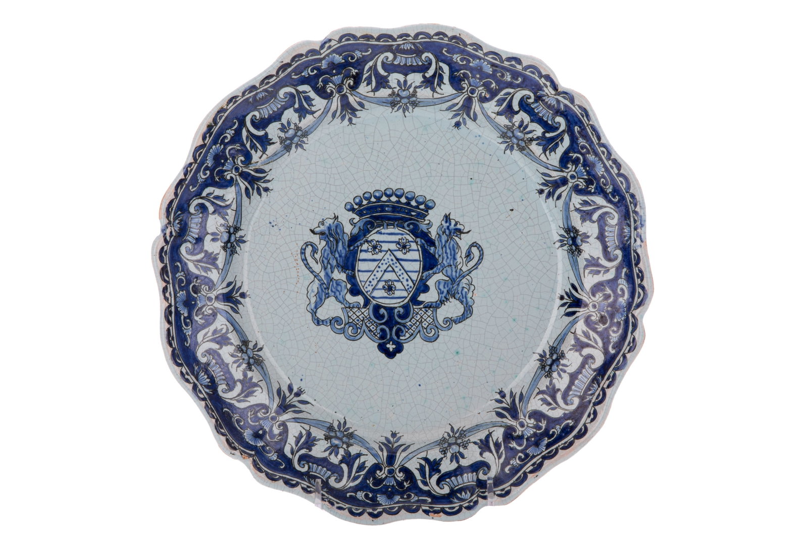 DELFTWARE BLUE & WHITE CRESTED CHARGER: A Delftware tin-glazed earthenware charger featuring a scalloped rim. The plate is decorated in a vibrant blue and white palette over a pale blue glazed ground. The central well features a prominent