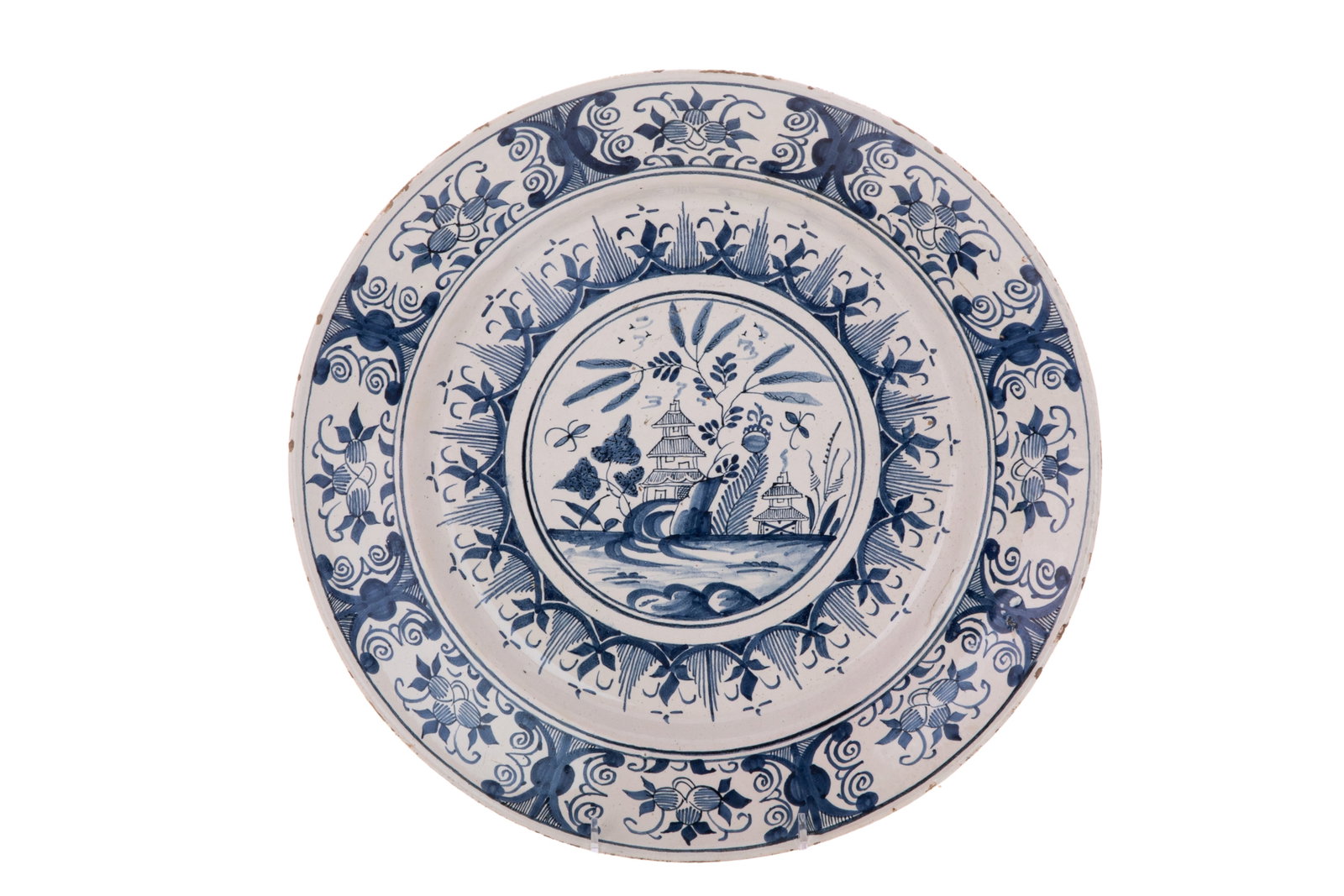DELFT GLAZED CHARGER, 18TH CENTURY: An 18th century Dutch Delft tin-glazed earthenware charger featuring a styled landscape motif depicting a central pagoda, willow trees, and water elements. The wide rim is decorated with a repeating