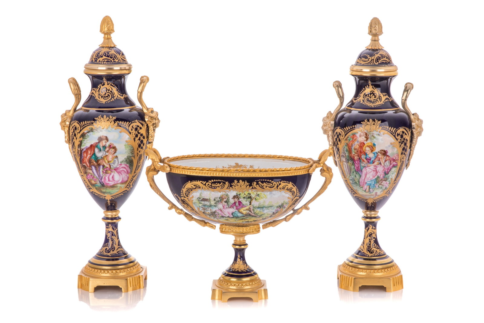 20TH C. S?VRES-STYLE THREE-PIECE GARNITURE: A three-piece French S?vres style gilt-metal mounted porcelain garniture set, 20th century. Includes one oval centrepiece and a pair of covered urns. Each piece features a deep cobalt blue ground, ric