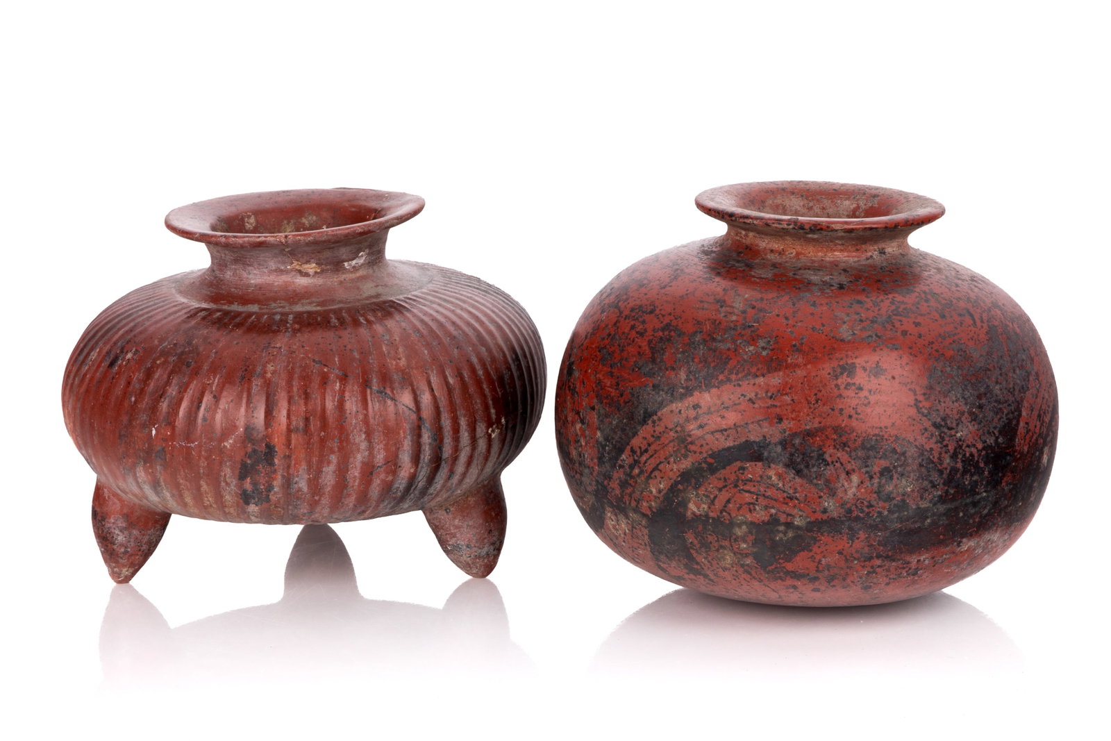 TWO PRE-COLUMBIAN VASES: A pair of pre-Columbian vases, one round with swirling patterns, the other is fluted along the swell of the body and has three feet. Fluted H. 7 3/4in x Dia. 10 1/4in (19.6cm x 26.1cm) H. 8 1/4in x Di