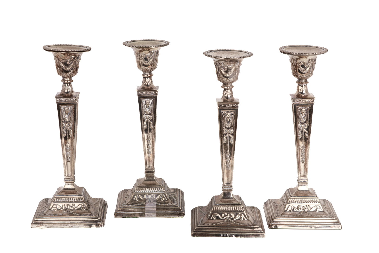 FOUR VICTORIAN NEOCLASSIC SILVERPLATE CANDLESTICKS: Each tapering square column decorated in relief with ram's heads and ribbons, removable sconce; each stamped J.P. & Co. H. 12 1/4in (31cm)