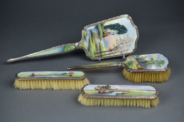 Fine enamel & silver plate vanity set: 4 piece set comprised of hand held mirror and three brushes. Each with landscape scene, probably English. L of mirror: 14 1/4 in.