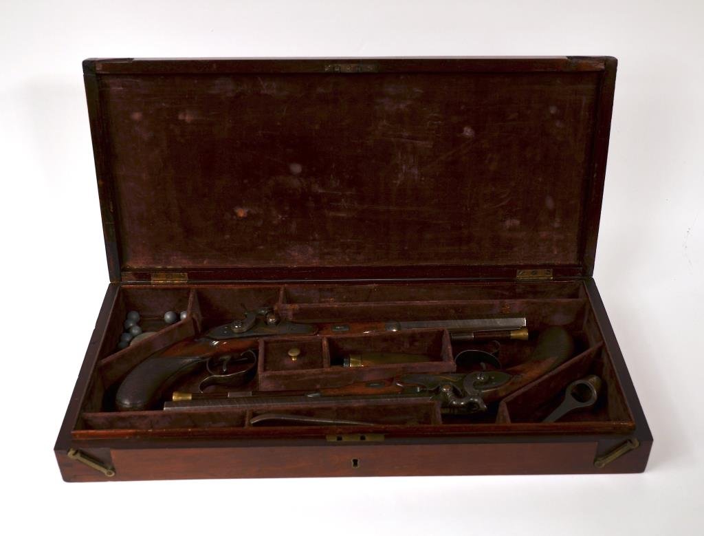 PAIR OF IRISH DUELING PISTOLS: Hardwood with crossed handle, engraved stell with gold inlay details and makers mark McDermott. Converted from flintlock to percussion, circa 1820. With a fitted case and implements. L of gun 40.5 cm.