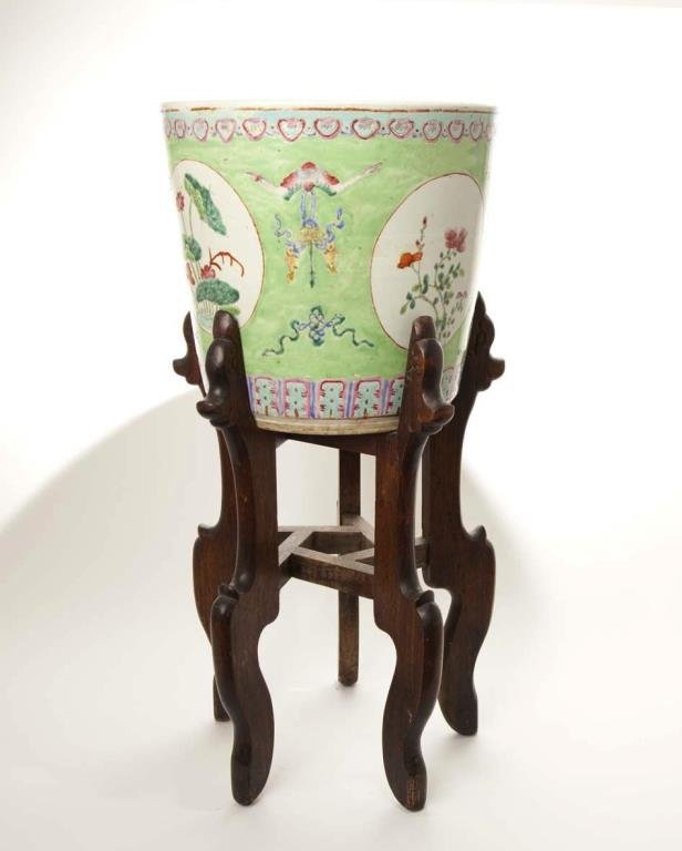 CHINESE FAMILLE ROSE PORCELAIN PLANTER: Painted on lime-green ground with cartouhes of flowers divided by bats with an ingot and fish in mouth, late 19th century. On carved fitted wood stands. H. 33.8cm (13 3/8 in.)