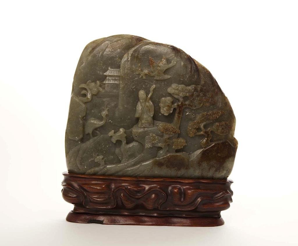 CHINESE CARVED GREEN JADE BOULDER: Carved to both sides a shoulau accompanied by cranes and a deer with fortune symbols of bat and lingzhi; the jade is with minor russet skin and white inclusions. On carved fitted wood stand. W. 21cm (