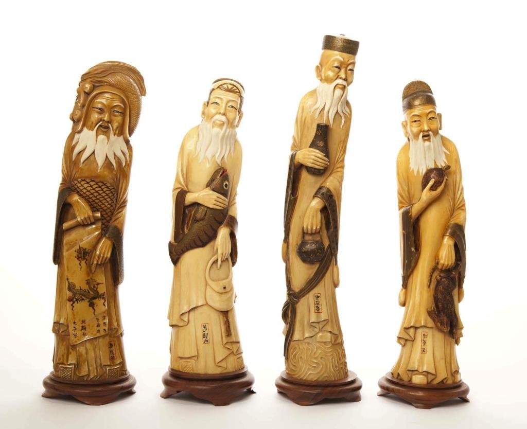 FOUR FINE JAPANESE CARVED IVORY DEITIES: Each elder is carved as with a turtle and a hare, a fish and a mesh, a vase and a teapot, and a scroll and a dragon fish. With maker's name, affixed to wood stands. Late 19th century Meiji period. Hig