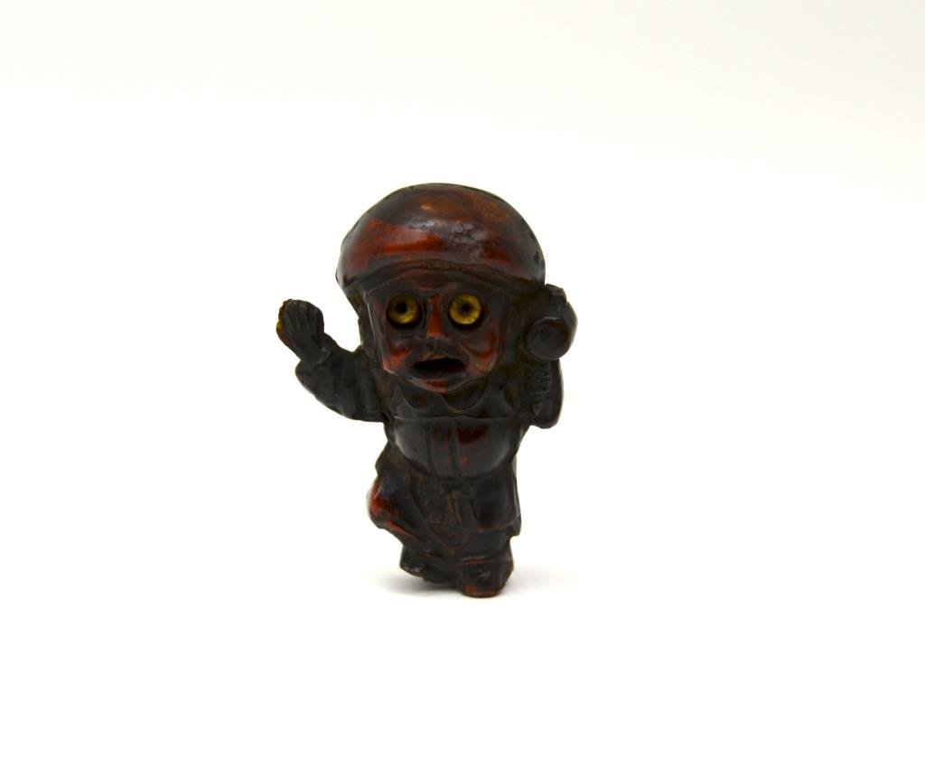 Japanese Carved Amber Okimono: As a boy with mobile eyes holding a pellet drum. 18th century or earlier. H. 5.5cm (2 1/4 in.) Very dense ancient amber, joined by two pieces, the tip of foot shows amber crystallization under light.