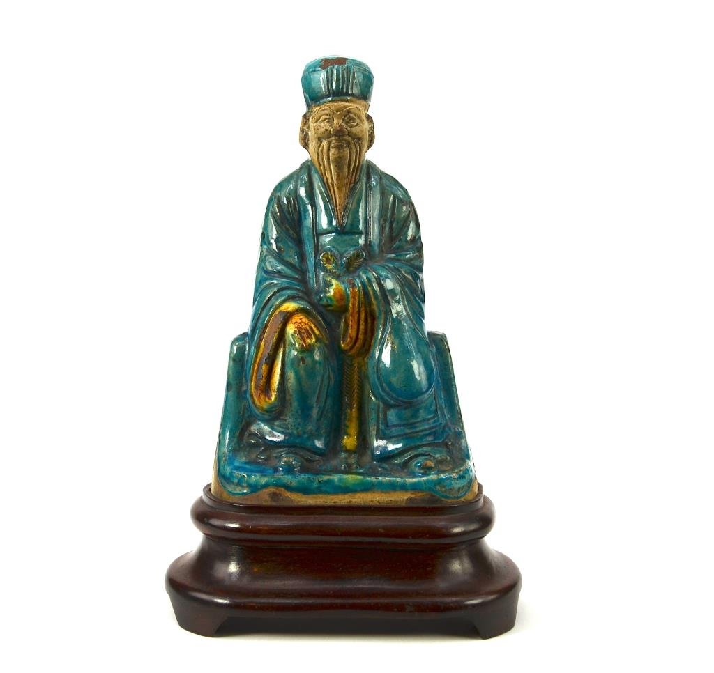 MING TURQUOISE GLAZED POTTERY FIGURE OF XUANWU: The daoist deity holds a cord in one hand, unglazed face and back. On fitted carved wood stand. H. 23cm (9 1/8 in.) No chip or crack, minor loss of glazing on robe and hat.