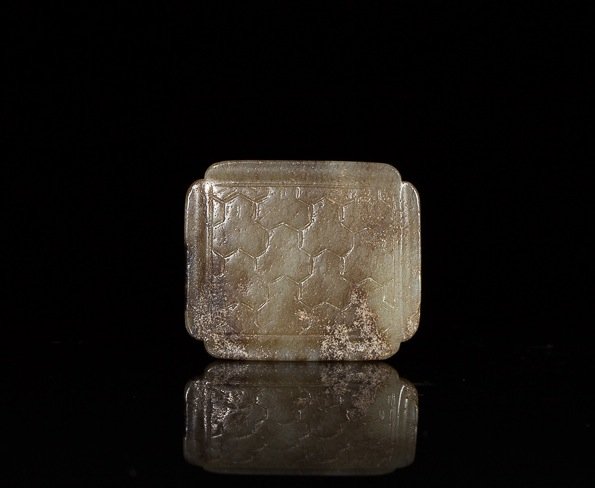GREEN-BROWN JADE ARCHAISTIC BELT PLAQUE: Squared form with a carved geometric scale pattern, piercing on verso. probably Han dynasty. W 4.5 cm. (1 3/4 in.) From the Irving Langleb collection, a prominent Jewish gentleman who resided in Japan