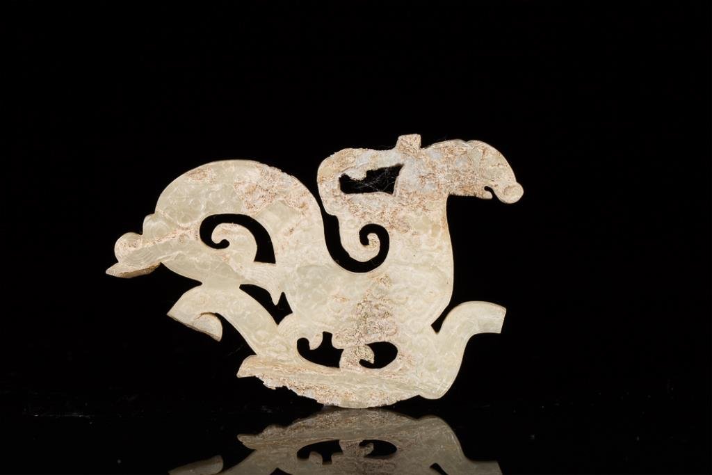 CALCIFIED WHITE JADE DRAGON PLAQUE FRAGMENT: Swirling body with an all over c-scroll or cloud decoration, probably Eastern Zhou. W 9.5 cm. (3 3/4 in.) From the Irving Langleb collection, a prominent Jewish gentleman who resided in Japan post-WWI