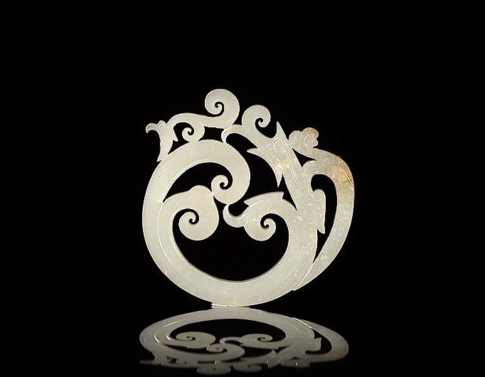 RARE WHITE JADE DRAGON RING PENDANT: Of a dragon in the round with carved scales and clouds, at the tail of the dragon is a small phoenix head, Ming dynasty. W 8.5 cm. (3 3/8 in.) From the Irving Langleb collection, a prominent Jewish ge