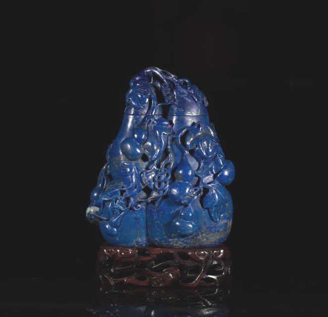 LARGE CARVED LAPIS LAZULI GOURD COVERED VASE: Finely carved twin double-gourd body decorated with more double-gourds as well as a cricket and leaf veins extending to the cover. On carved fitted wood stand. H. 20.5cm (8 1/8 in.)