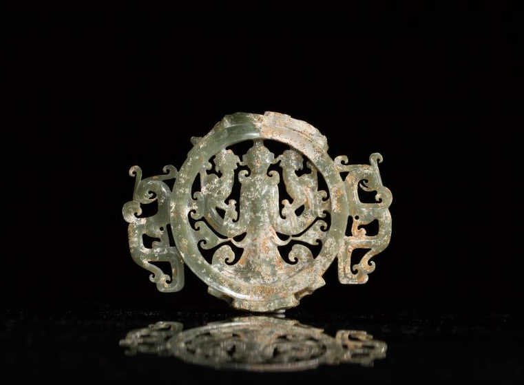 CARVED CHICKEN BONE CELADON JADE PLAQUE: Carved and pierced in the Song/Ming maneer, the circular plaque depicts a goddess flanked by two phoenixes, with double stylized qilin handles. W. 9.7cm (3 7/8 in.)