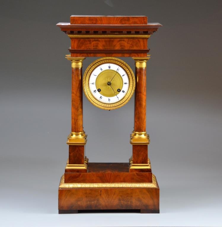 FRENCH EMPIRE FLAME MAHOGANY PORTICO CLOCK: Classical form with four ormolu mounted columns supporting an enamel dial, 19th c. H. 62 cm (24 1/2 in.)