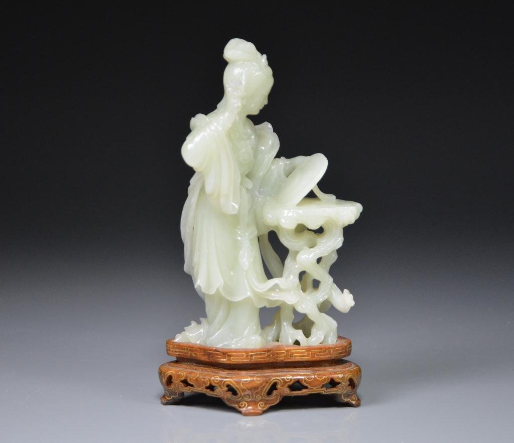 FINELY CARVED CELADON JADE FIGURE: A beauty holding a hand mirror. On carved fitted wood stand. H. 15.3cm (6 in.)