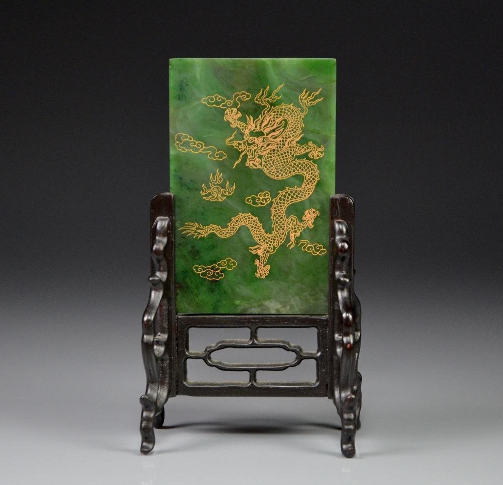 CHINESE SPINACH GREEN JADE DRAGON PLAQUE: Beautiful swirled and feathered inclusions, front of the plaque with a gold painted five claw dragon surrounded by clouds and fire. On a fitted hardwood stand. Jade: 14 x 9 cm. (5 1/2 x 3 1/2 in.)